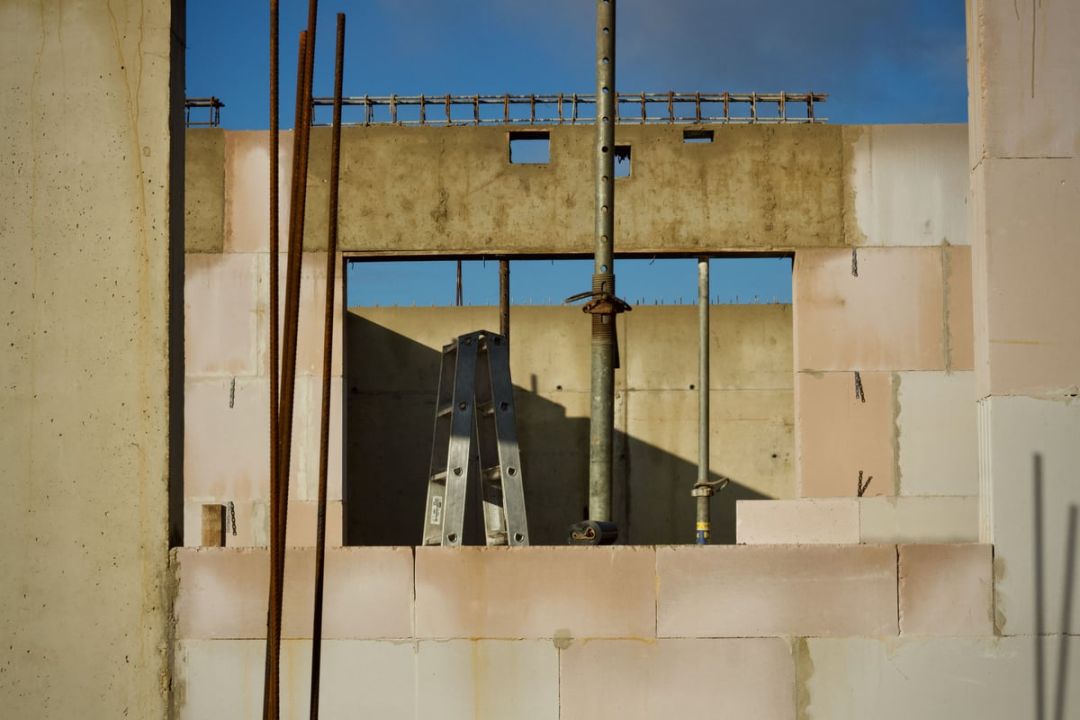 Fensteröffnung in einer Mauerwerkswand, darüber ein betonierter Ringanker mit Anschlussbewehrung, dahinter zwei Baustützen