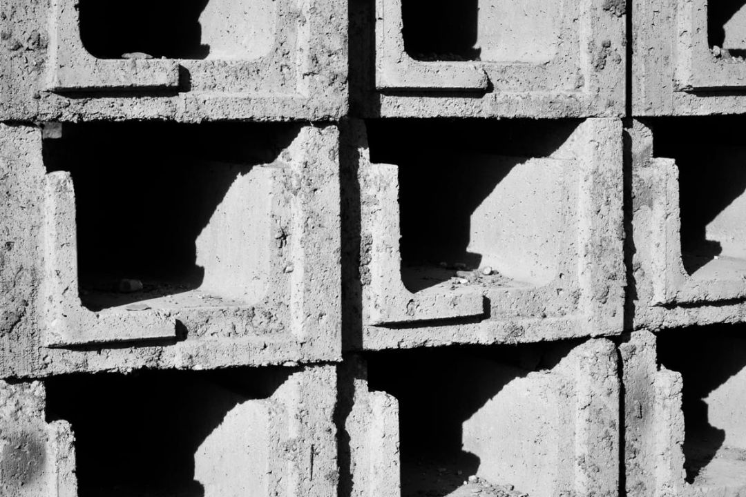Gestapelte Betonfertigteile mit rechteckigen Aussparungen, hartes Streiflicht zeichnet die Kanten nach