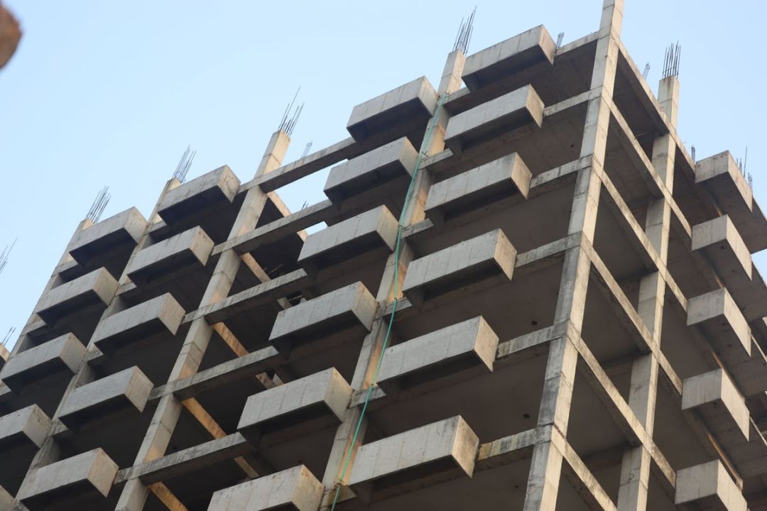 Rohbau eines Betonskeletts von unten gesehen, mit Stützen, auskragenden Deckenplatten und aufgehender Bewehrung